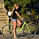 woman in black tank top and blue denim shorts standing beside green bicycle during daytime